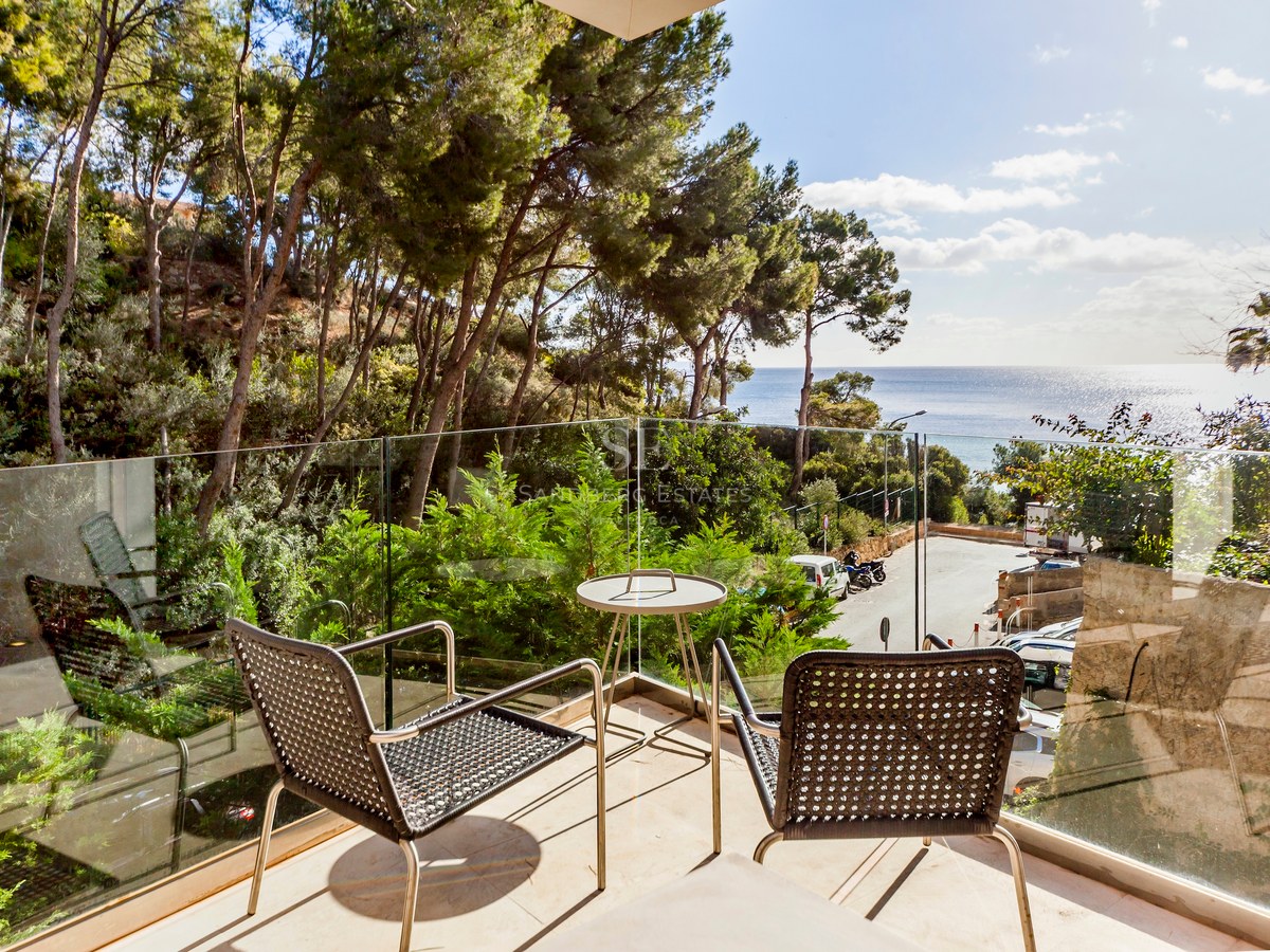 Terrasse avec garde-corps en verre et mobilier moderne donnant sur une pinède et la mer Méditerranée.