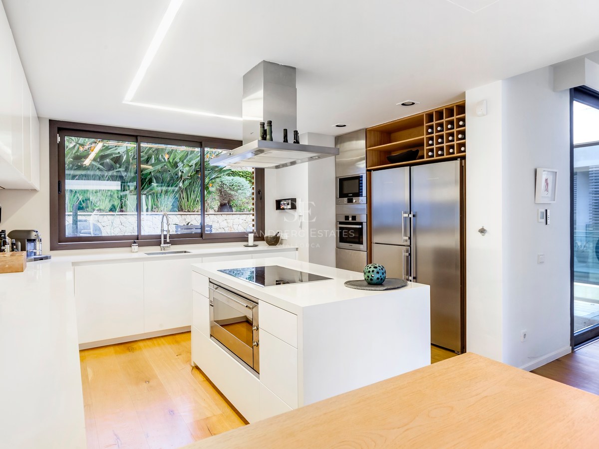 Cuisine blanche moderne avec îlot central, appareils en acier inoxydable et parquet en bois avec vue sur le jardin.