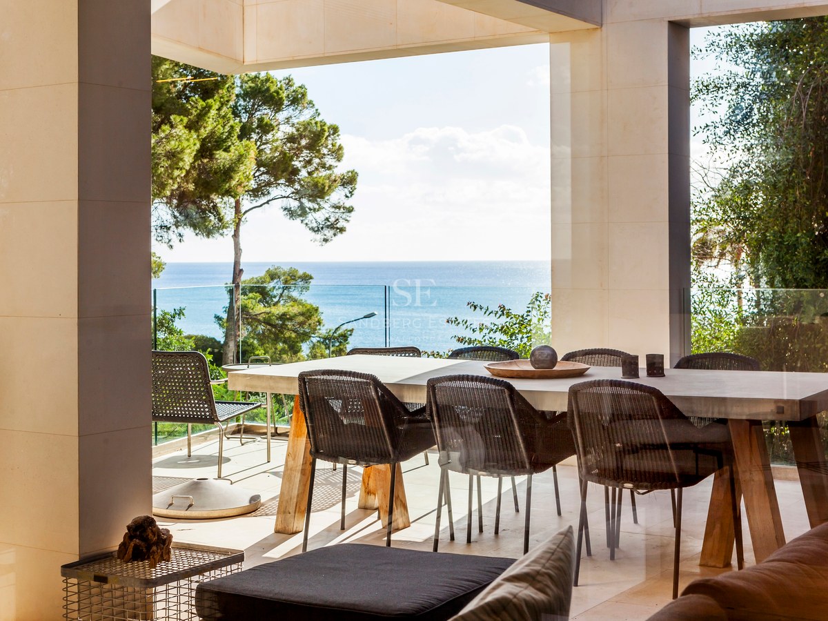 Espace dînatoire extérieur sur une terrasse en pierre avec garde-corps en verre et vue sur la Méditerranée.