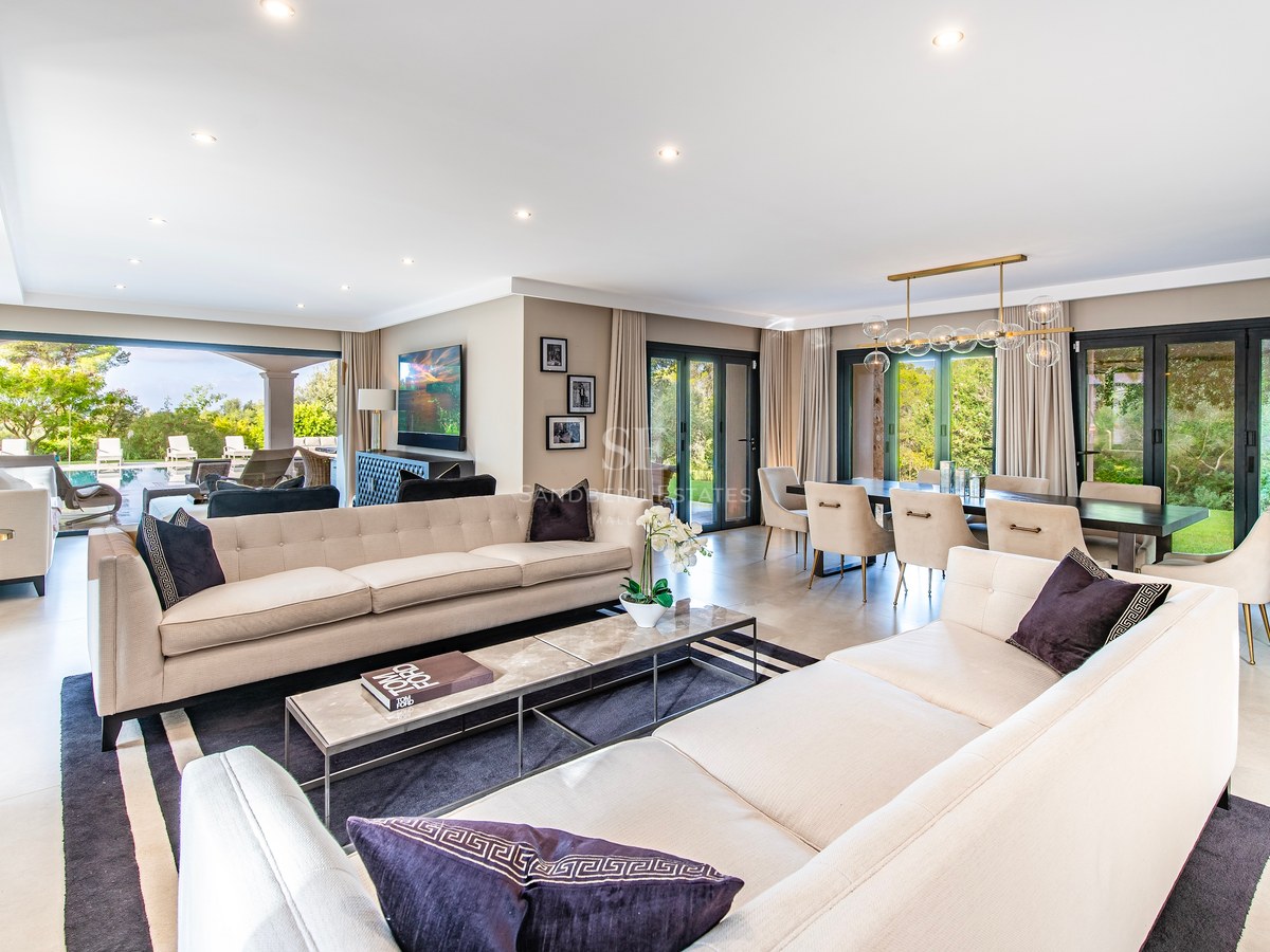 Salón espacioso y contemporáneo con sofás color crema, mesa de mármol y ventanales que dan al jardín.