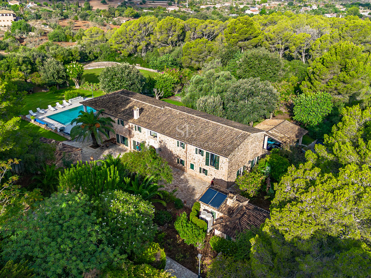Vista aérea de una gran casa de campo de piedra y piscina rodeada de un denso bosque de pinos verdes.