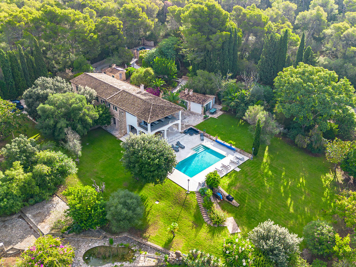 Vista aérea de una gran villa de piedra rodeada de bosque, con piscina turquesa y amplios jardines verdes.
