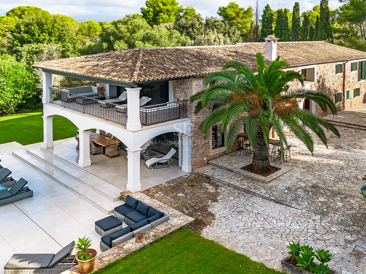 Vista aérea de una villa de piedra con arcos blancos, terrazas exteriores, una palmera y zona de piscina.