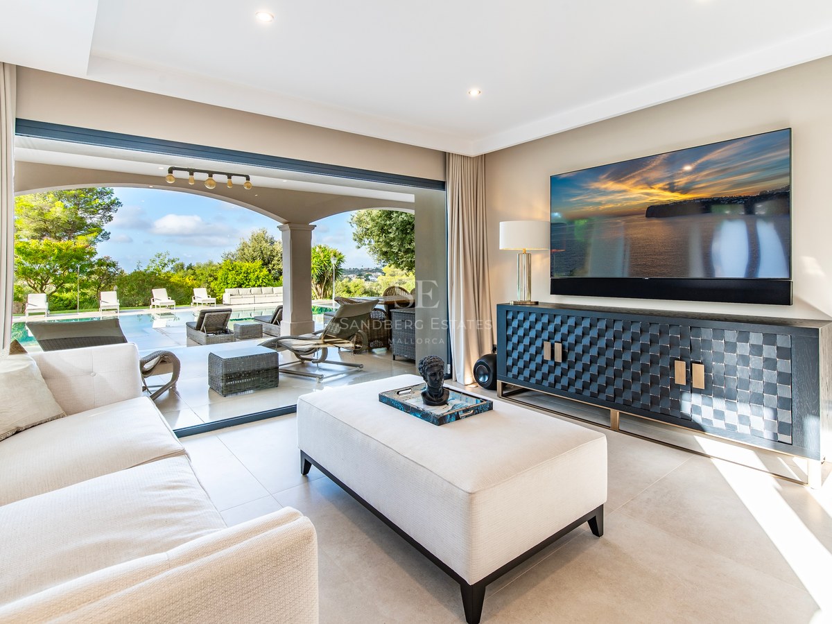 Amplio salón moderno con sofá crema, aparador de diseño y grandes ventanales que dan a la piscina y terraza.