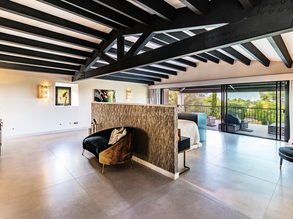 Dormitorio principal moderno con vigas oscuras, terraza privada y muebles de diseño bajo luz natural.