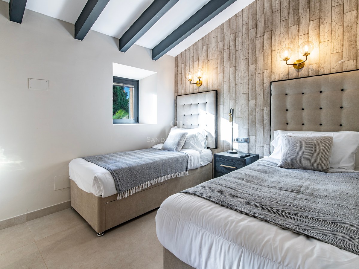 Dormitorio contemporáneo con dos camas individuales, cabeceros tapizados, pared de madera y vigas oscuras en el techo.
