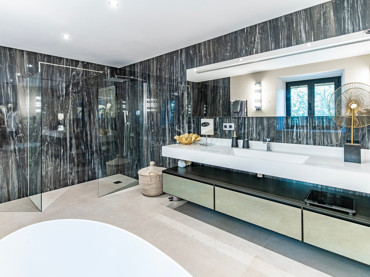 Baño de lujo con paredes de mármol oscuro, ducha de obra acristalada y lavabo doble suspendido.