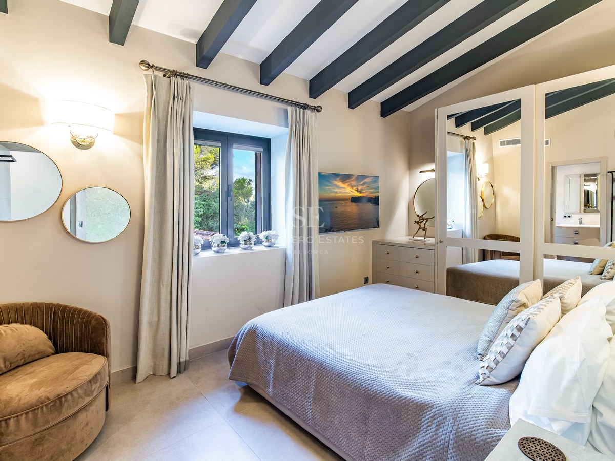 Dormitorio con cama doble, vigas de madera oscura, armario de espejos y ventana con vistas al jardín.