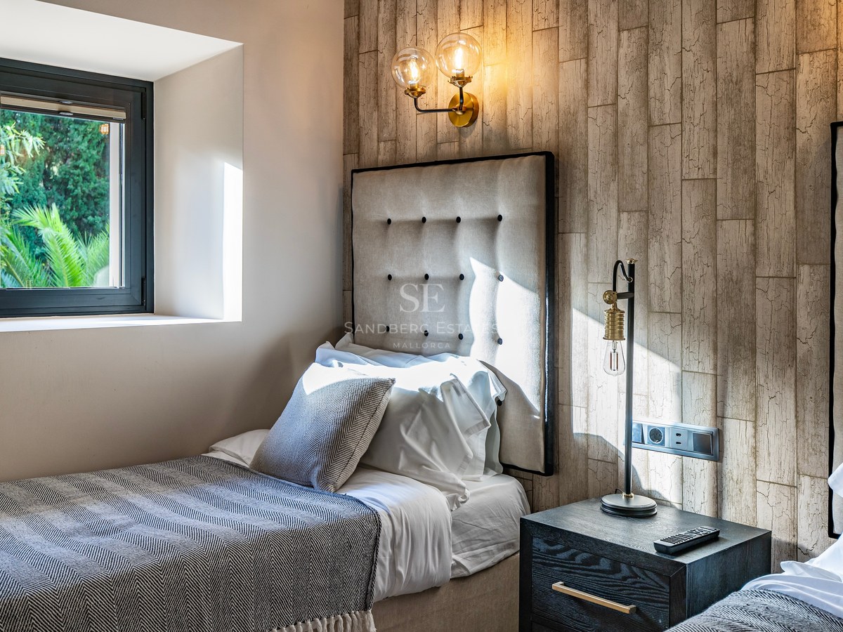 Dormitorio moderno con dos camas, cabecero de tela acolchado, pared con textura de madera y lámparas industriales.