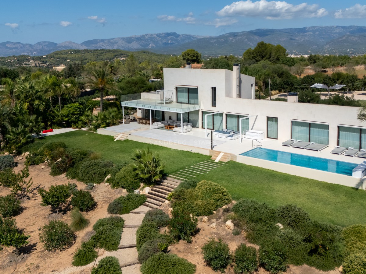 Vista exterior de villa moderna con piscina infinita, amplios ventanales y jardines exuberantes. Arquitectura minimalista.