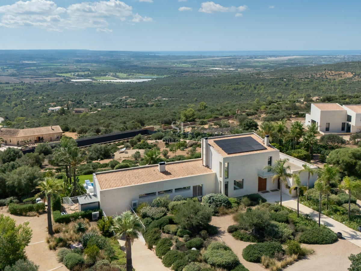 Vista de piscina infinita y jardín exuberante. Arquitectura moderna con amplios ventanales y terraza amueblada. Diseño elegante y sofisticado.