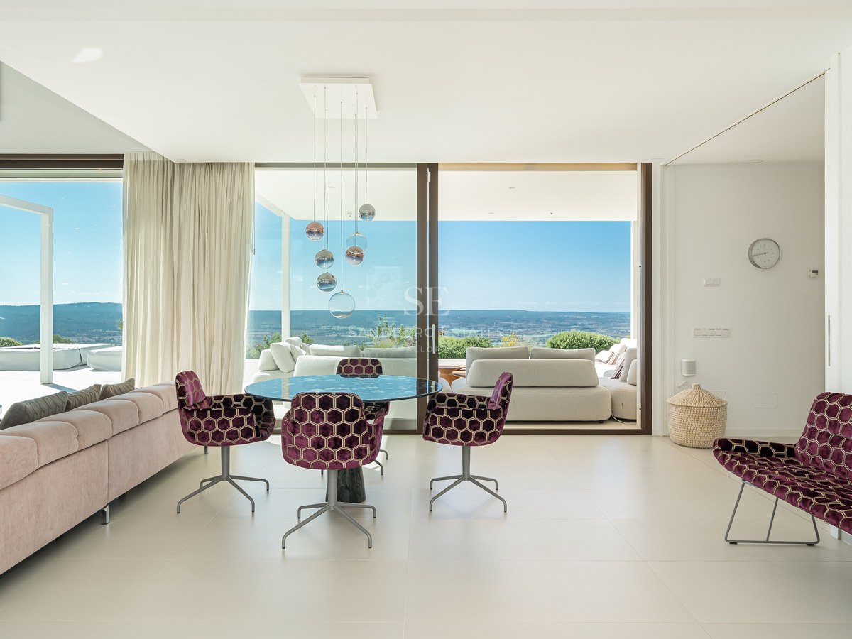 Vista exterior de una villa moderna con piscina infinita, tumbonas y exuberante jardín. Arquitectura minimalista con amplias ventanas.