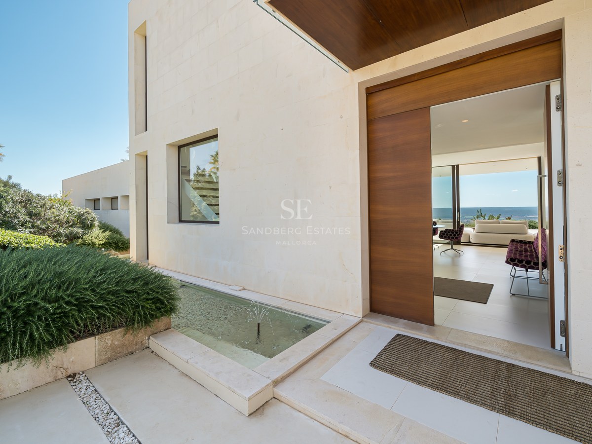 Vista exterior de una moderna casa con piscina, amplios ventanales, terraza de madera y exuberante vegetación. Arquitectura minimalista.