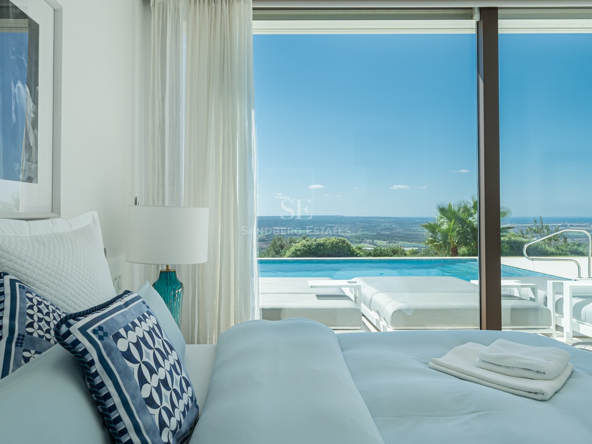 Vista de una piscina moderna rodeada de vegetación exuberante y una casa con grandes ventanales y diseño minimalista.