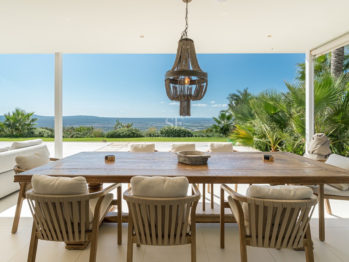 Vista de una piscina moderna rodeada de vegetación exuberante y una casa con grandes ventanales. Diseño minimalista.