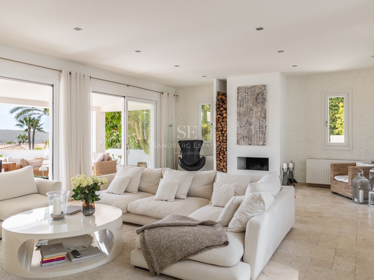 Grand salon aux tons crème avec sol en travertin et baies vitrées ouvrant sur une terrasse ensoleillée.
