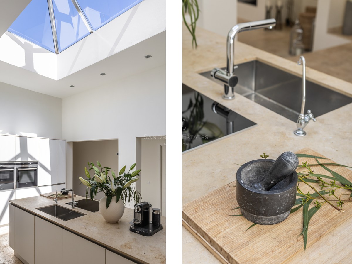 Îlot de cuisine avec plan de travail en pierre naturelle sous un grand puits de lumière en verre et appareils intégrés.