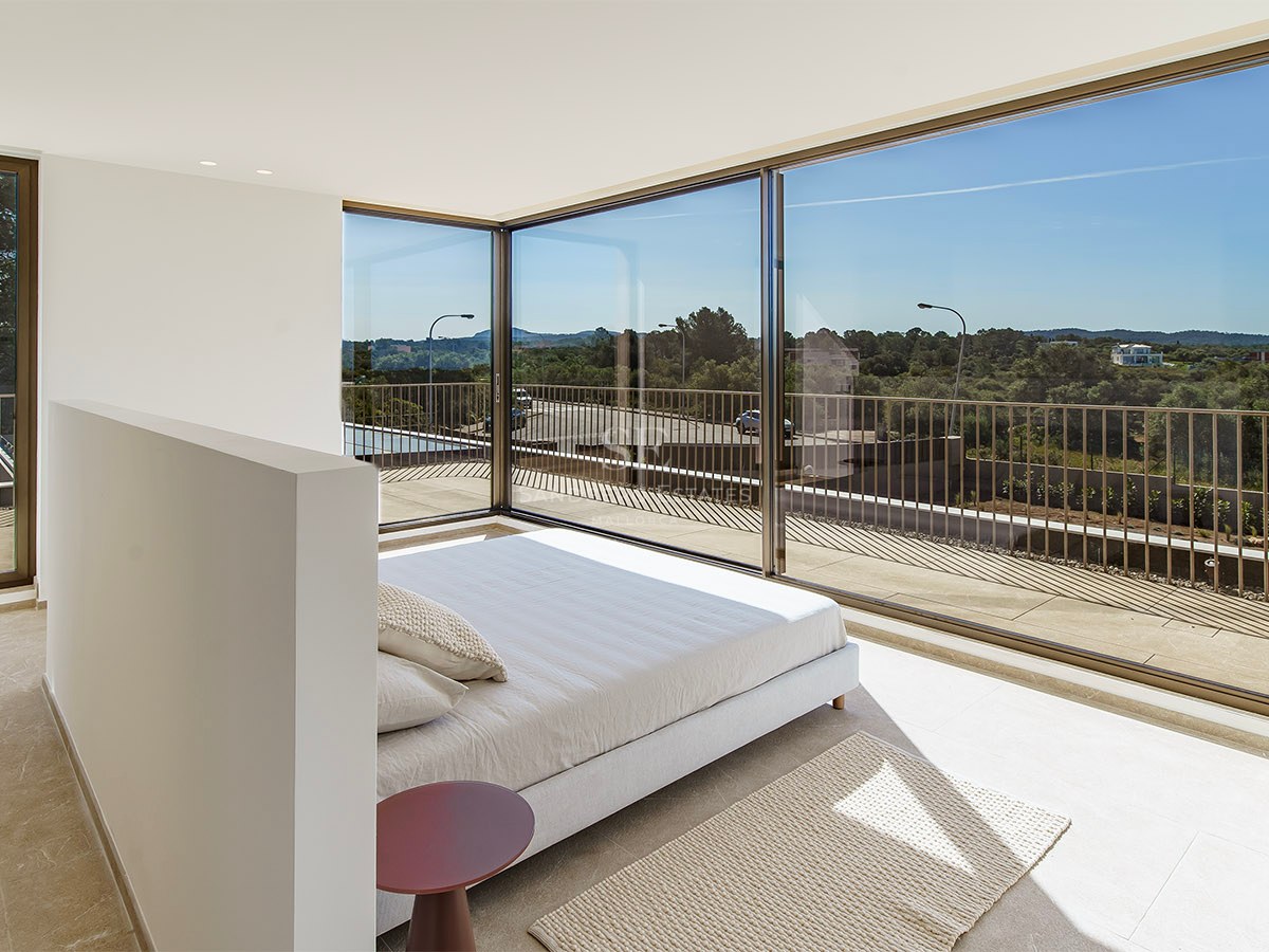 Chambre minimaliste avec baies vitrées toute hauteur offrant une vue sur le paysage verdoyant et la terrasse.