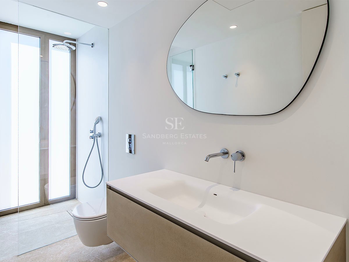 Salle de bain moderne dotée d'un miroir de forme organique, d'un meuble vasque blanc et de robinets chromés encastrés.