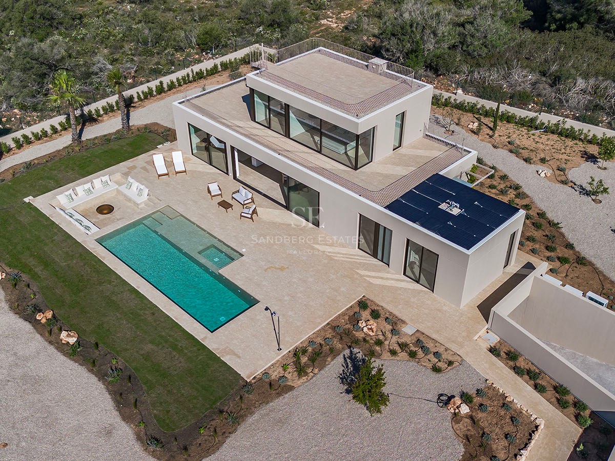 Vue aérienne d'une villa blanche moderne avec piscine turquoise, grande terrasse en pierre et jardin paysager.