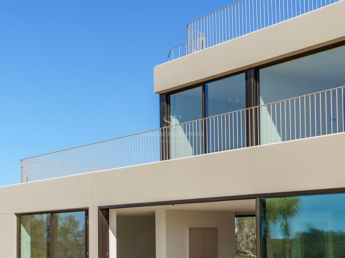 Façade d'une villa contemporaine beige avec de grandes fenêtres en verre et des garde-corps en métal minimalistes.