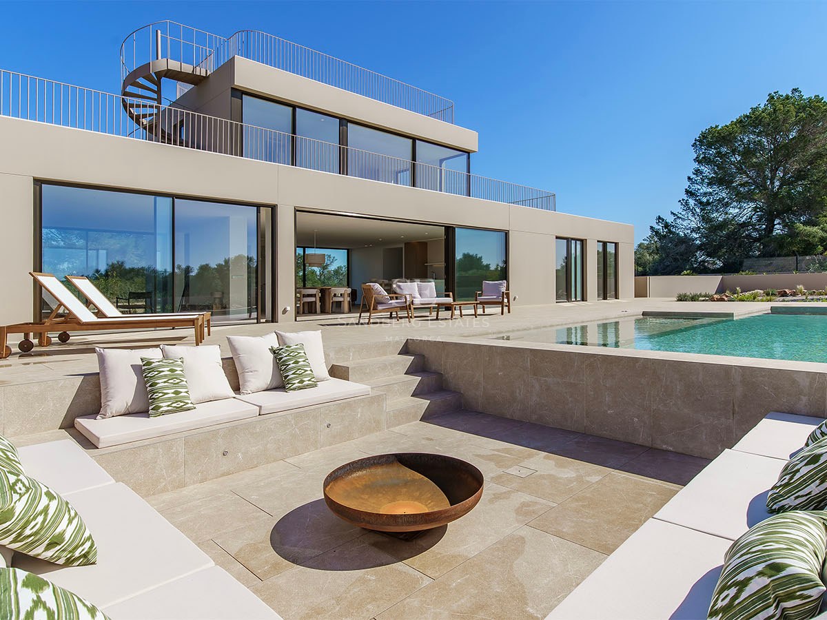 Extérieur d'une villa moderne à deux étages avec un salon encastré et un brasero à côté d'une piscine turquoise.