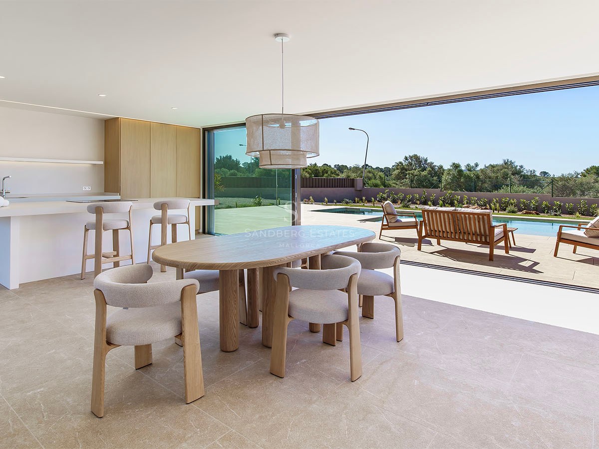 Espace dînatoire en bois clair avec baies vitrées ouvertes sur une terrasse et une piscine ensoleillée.