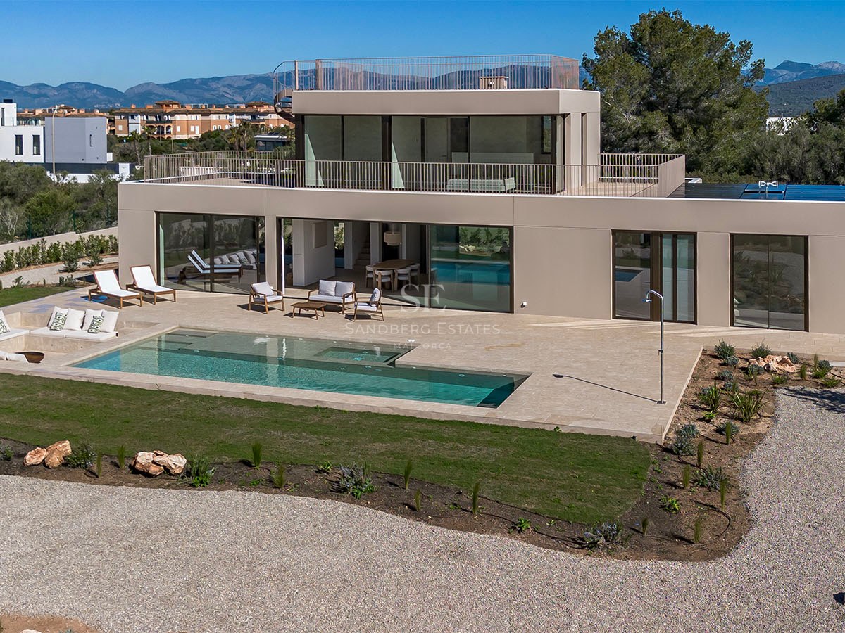 Façade d'une villa contemporaine avec piscine rectangulaire, grande terrasse en pierre et baies vitrées.