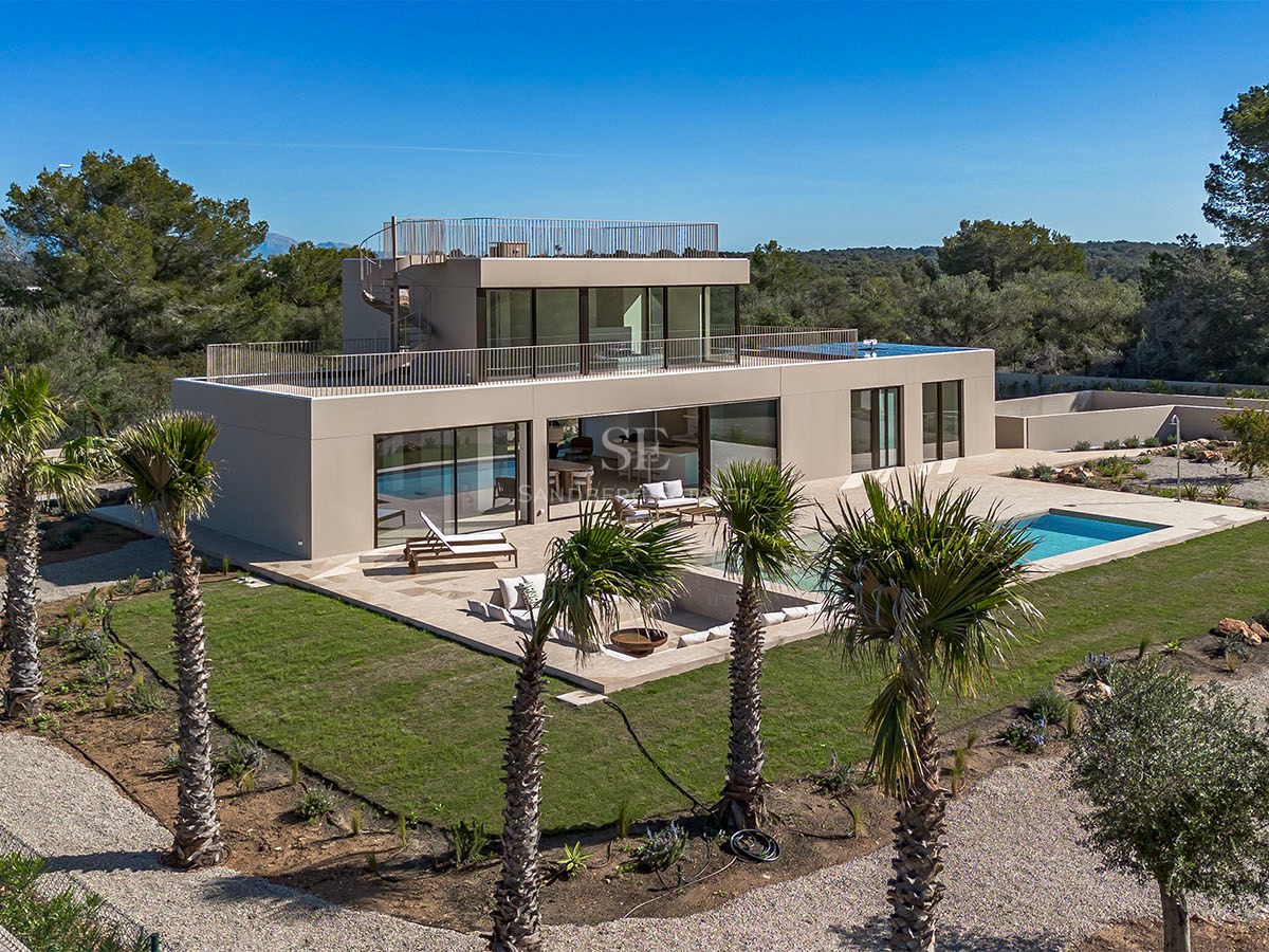 Vue d'une villa contemporaine à deux étages avec piscine, pelouse et balcons en verre sous un ciel bleu.