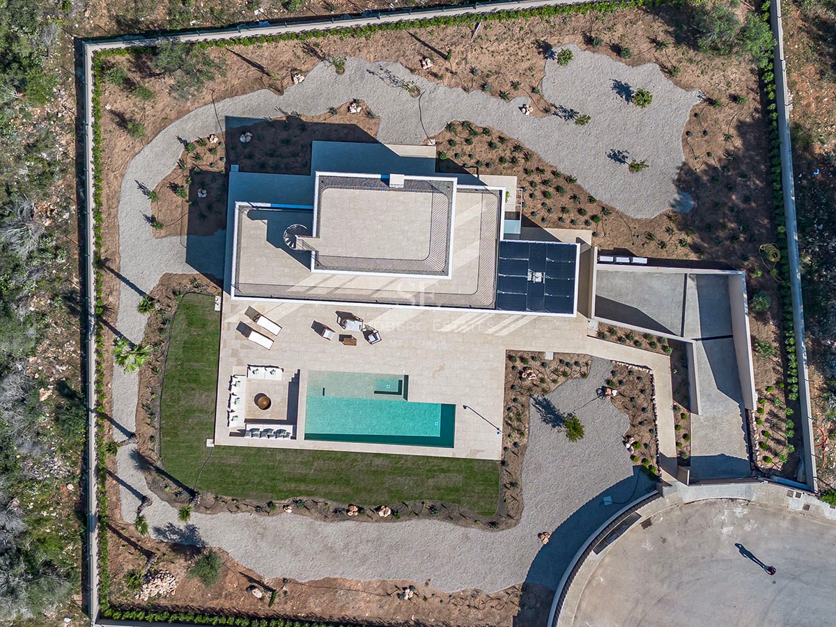 Vue par drone d'une villa contemporaine avec piscine rectangulaire, jardin paysager et terrasse géométrique.