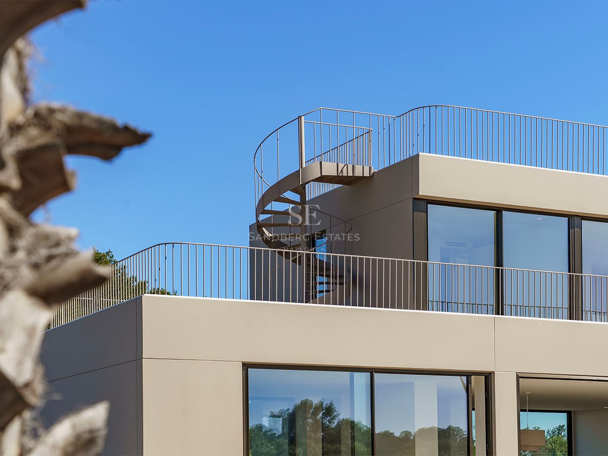 Détail architectural d'une villa beige contemporaine avec un escalier en colimaçon menant au toit sous un ciel dégagé.