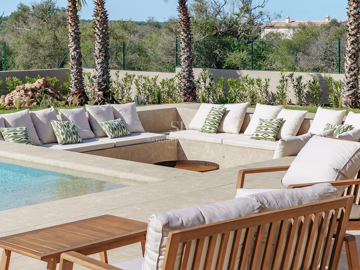 Salon d'été encastré en pierre naturelle avec mobilier en bois à côté d'une piscine et de palmiers.