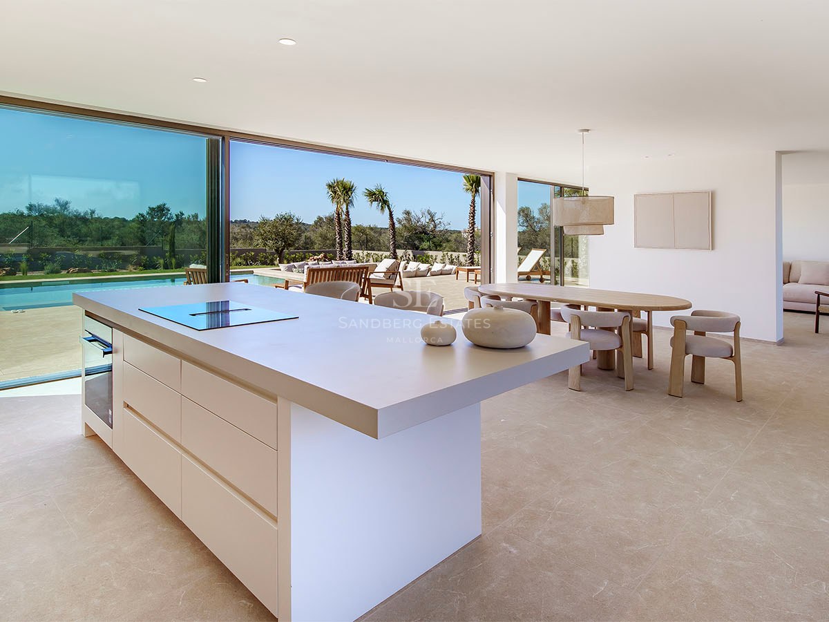 Îlot de cuisine moderne et salle à manger avec baies vitrées s'ouvrant sur une terrasse ensoleillée avec piscine.