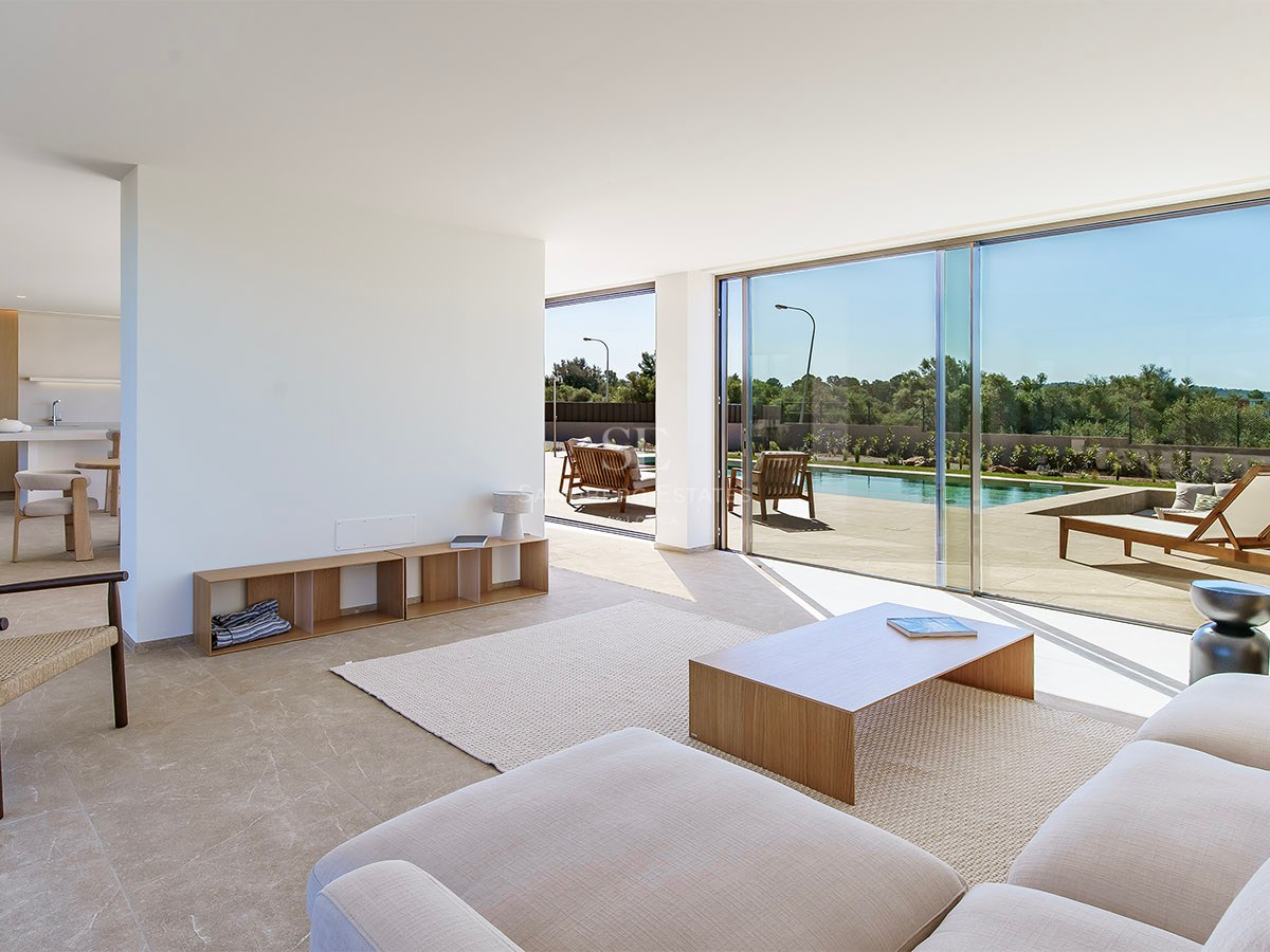 Salon lumineux minimaliste avec baies vitrées ouvrant sur une terrasse ensoleillée et une piscine.