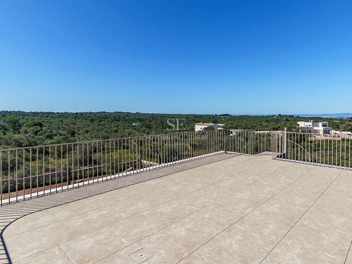 Terrasse en pierre avec garde-corps métallique surplombant un paysage verdoyant sous un ciel bleu azur.
