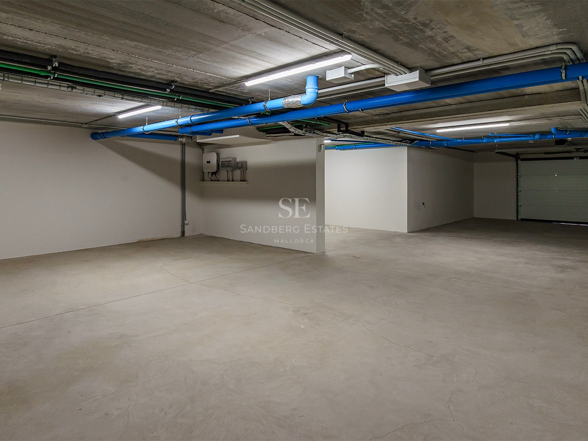 Garage souterrain vide avec sols en béton, tuyaux bleus et murs blancs sous éclairage LED.
