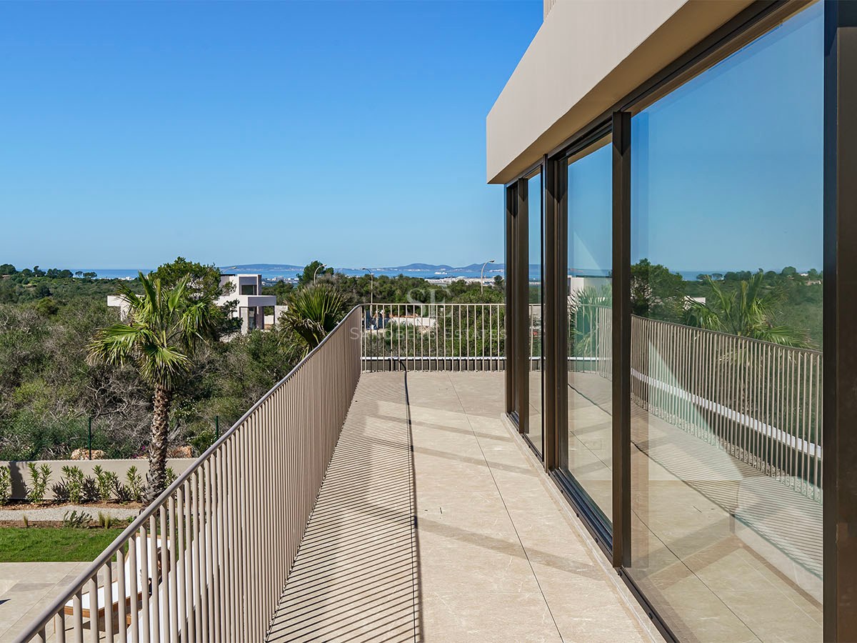 Balcon contemporain avec baies vitrées, garde-corps métallique et vue mer sous un ciel bleu clair.