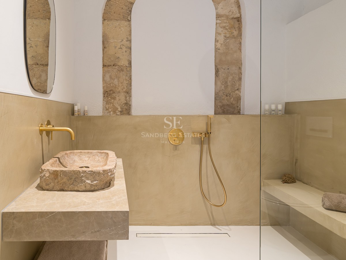 Salle de bain moderne avec vasque en pierre brute, robinetterie dorée et douche à l'italienne avec arche en pierre.