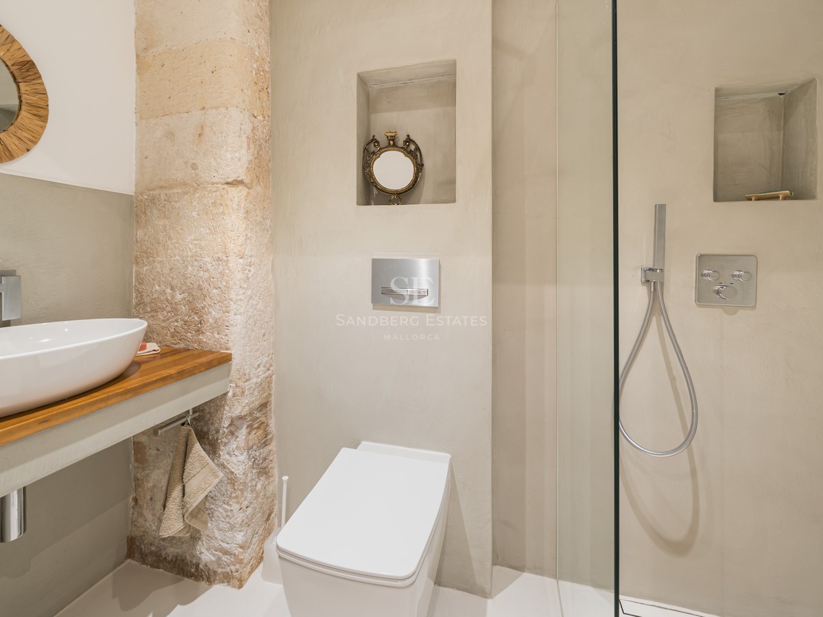 Salle de bain moderne avec vasque blanche, plan en bois, pilier en pierre et douche vitrée.