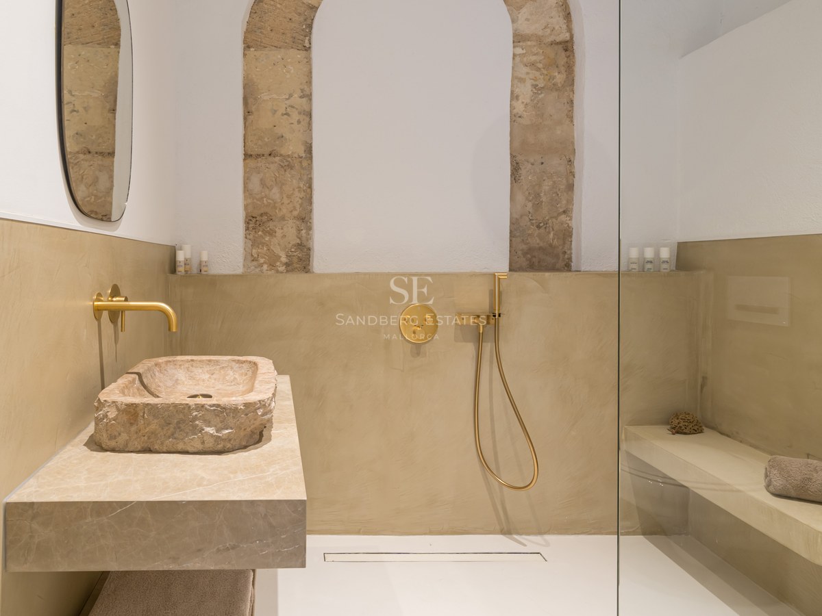 Salle de bain moderne avec une vasque en pierre brute, robinetterie dorée et douche à l'italienne vitrée.