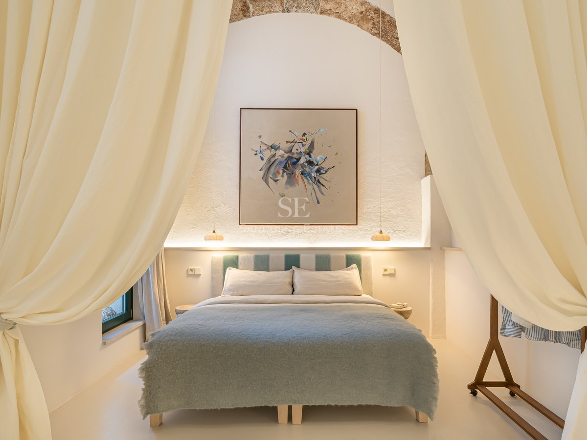 Chambre élégante avec arche en pierre, art abstrait et literie bleu doux encadrée par de grands rideaux crème.