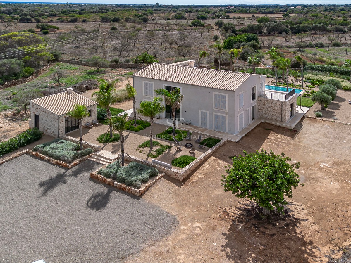 Vue aérienne d'une villa contemporaine beige avec piscine et jardin paysager dans la campagne majorquine.