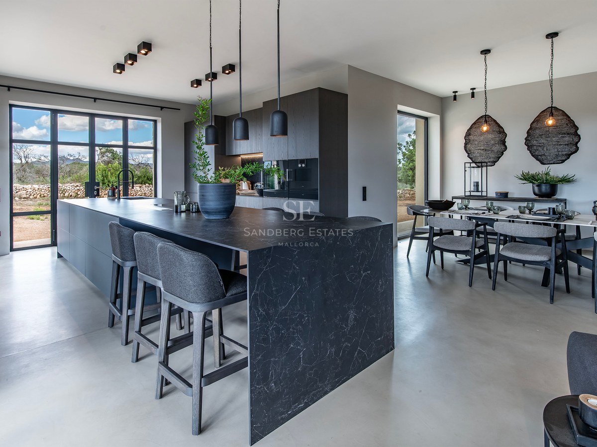 Cuisine ouverte moderne avec îlot en marbre noir, tabourets gris et espace salle à manger sous des suspensions design.