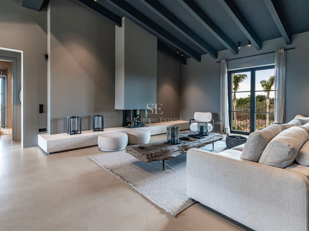 Grand salon moderne avec poutres grises, canapé beige, table en bois rustique et cheminée intégrée minimaliste.