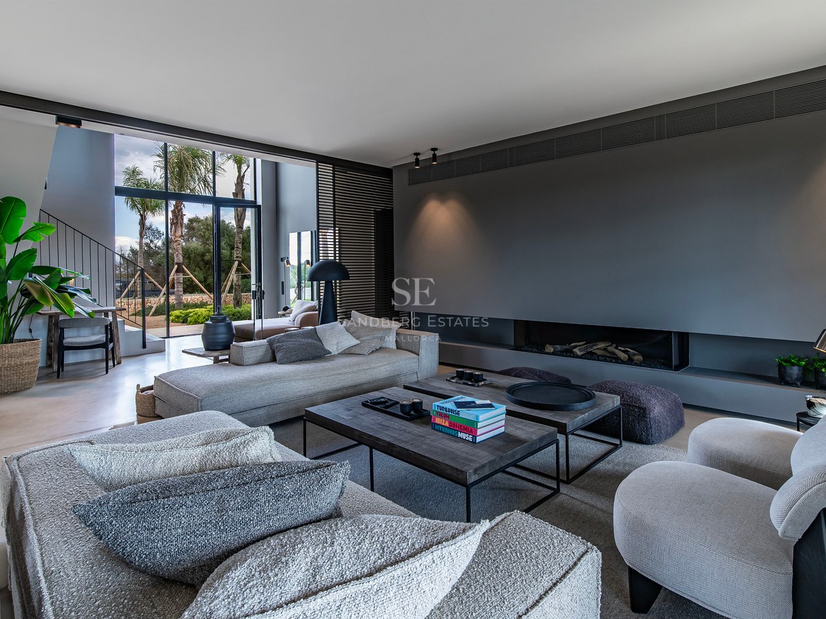 Grand salon moderne avec canapés gris, cheminée intégrée et grandes baies vitrées donnant sur des palmiers.