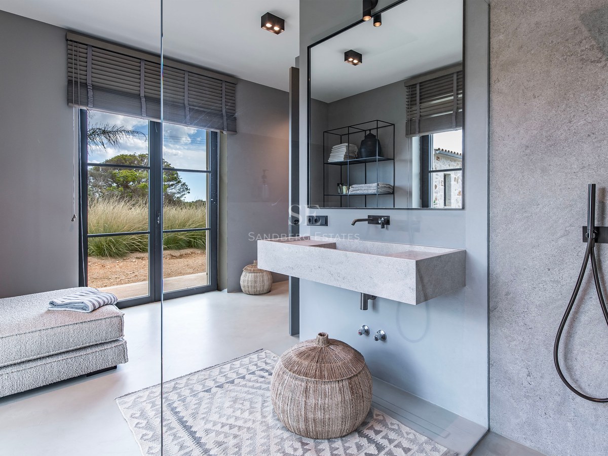 Salle de bains moderne avec vasque suspendue en pierre, robinetterie noir mat et porte vitrée donnant sur le jardin.