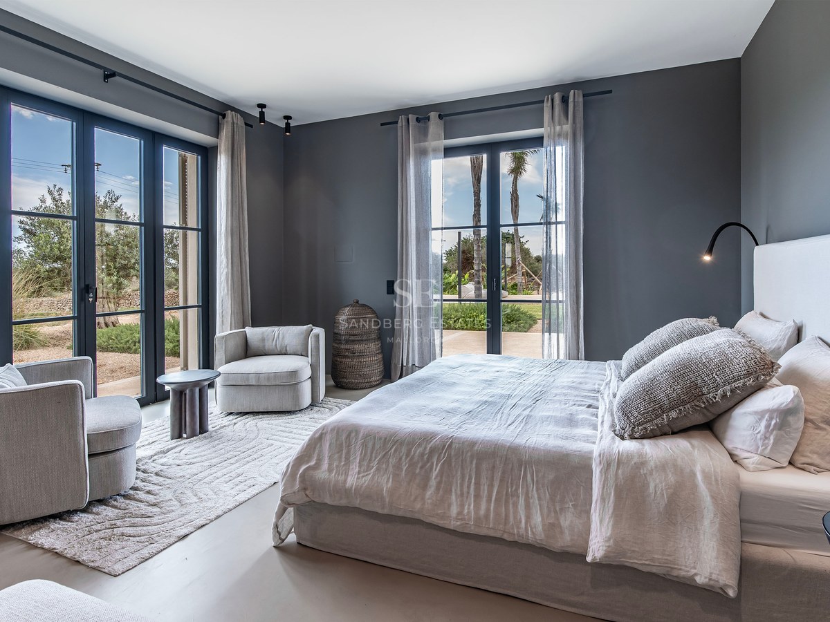 Chambre élégante aux murs gris, grand lit, fauteuils et baies vitrées ouvrant sur l'extérieur.