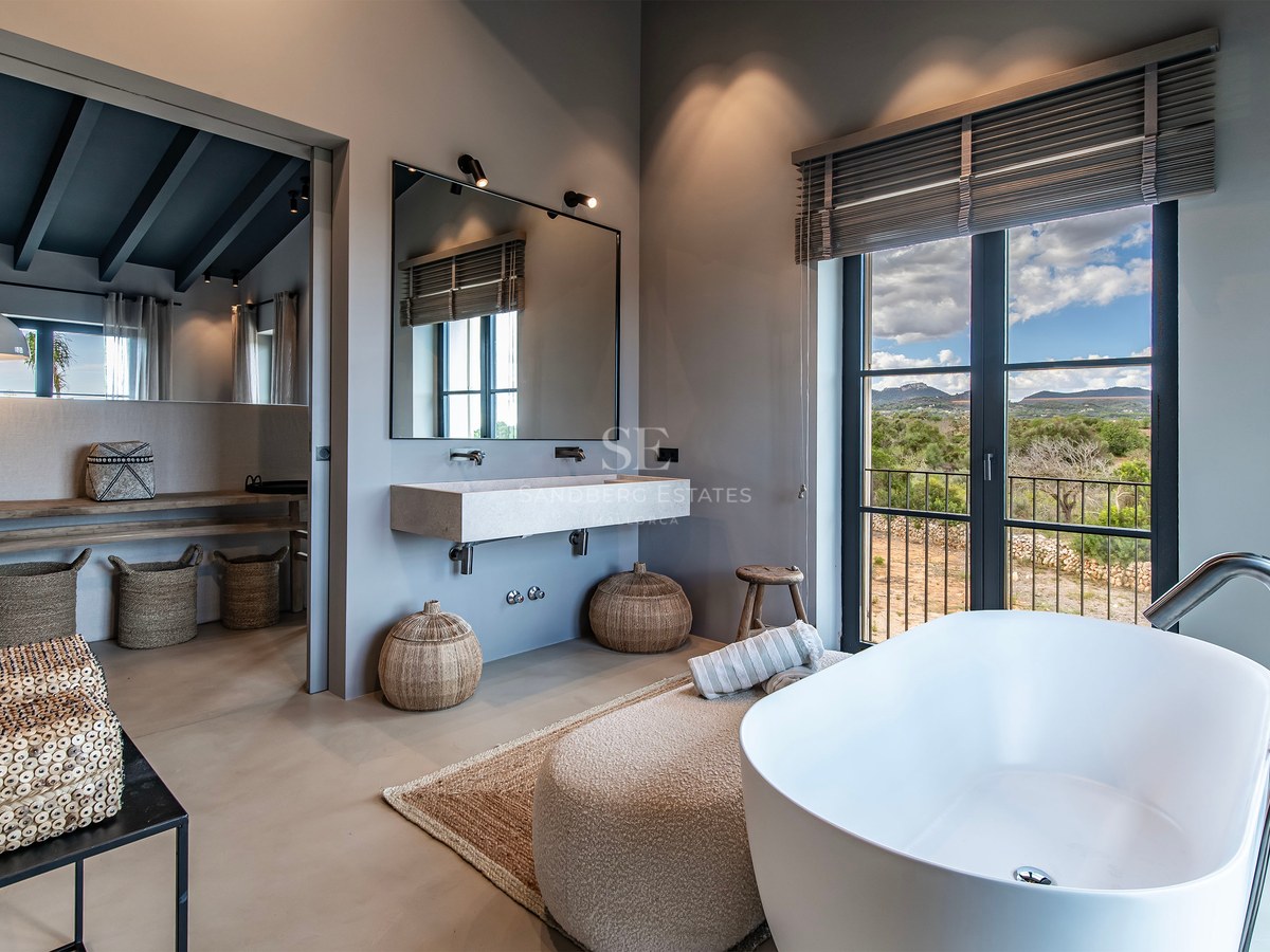 Salle de bain moderne avec baignoire îlot, lavabo suspendu et grande fenêtre donnant sur un paysage de montagne.