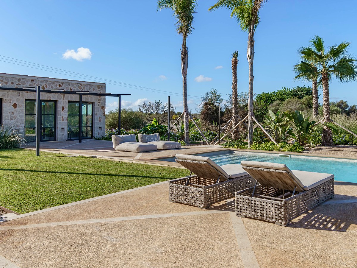 Piscine de luxe avec bains de soleil, palmiers et pavillon en pierre naturelle sous un ciel dégagé.
