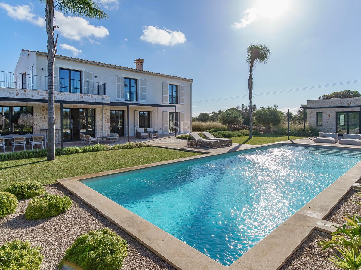 Villa de luxe en pierre avec grande piscine rectangulaire, pelouse impeccable et palmiers sous un soleil éclatant.